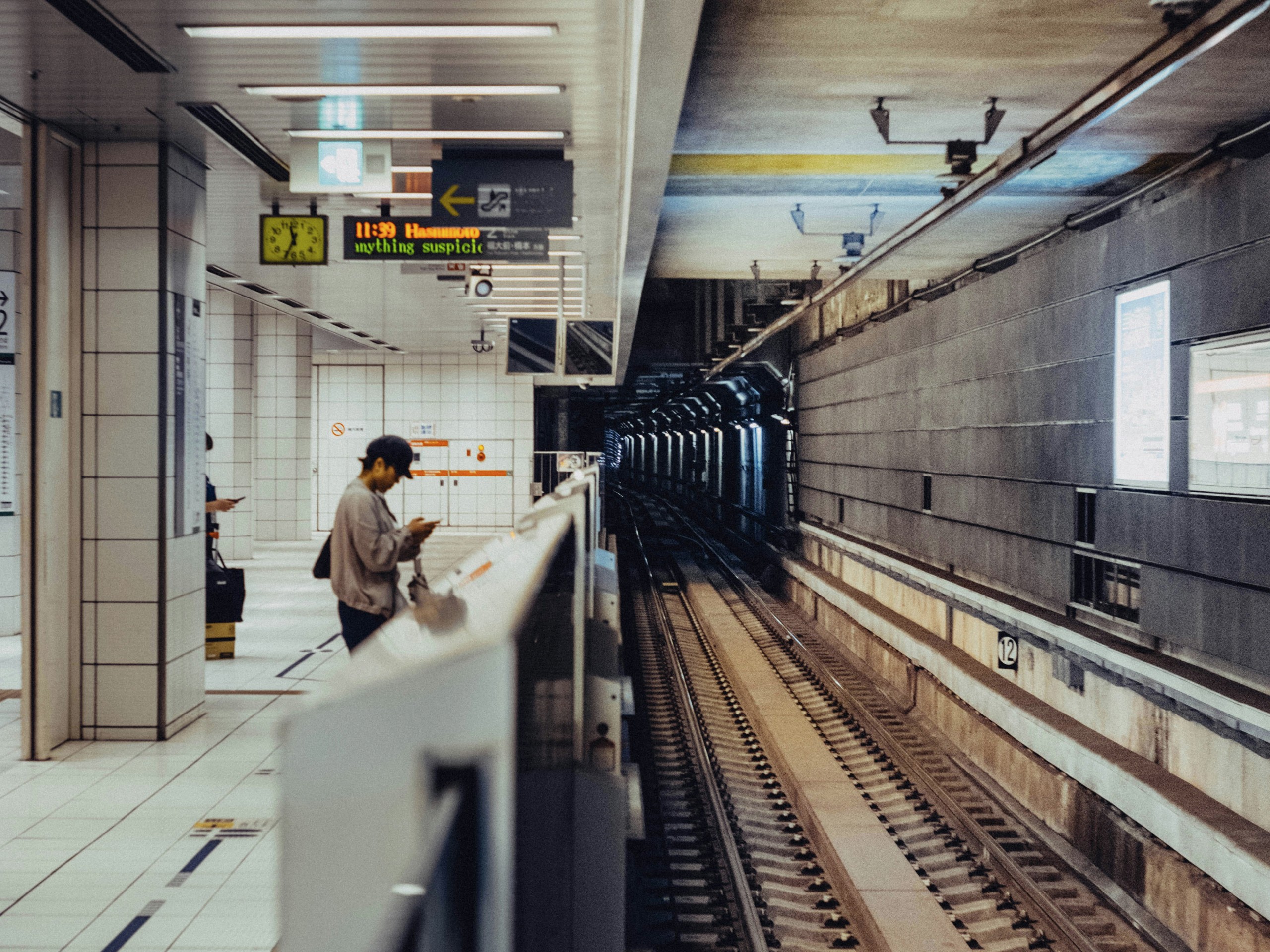 地下鉄のホームでスマートフォンを見つめる男性と、暗く伸びる線路の奥行き