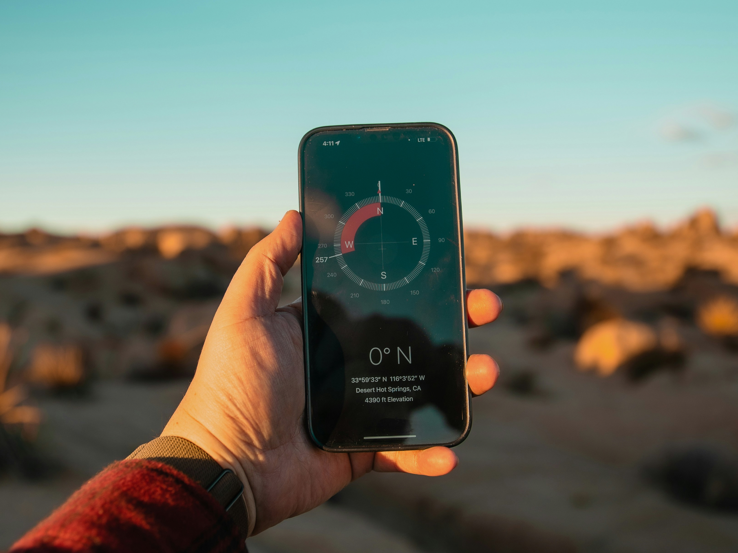 手に持ったスマートフォンのコンパスアプリ。探索の方向を示すように砂漠の風景を背景に表示されている。